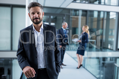 Businessman standing in office corridor and colleagues talking in background
