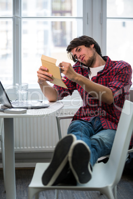 Graphic designer talking on mobile phone and writing in a diary at his desk