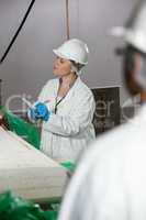 Female technician writing on notepad while examining meat processing machine