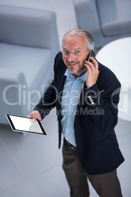 Businessman with digital tablet looking up while talking on his phone