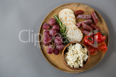 Crispy biscuits, cherry tomatoes, grapes and bowl of cheese on wooden board