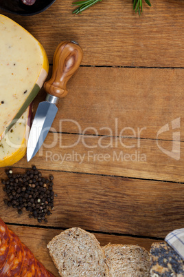 Cheese, knife, black pepper and bread on chopping board