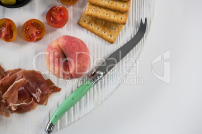 Meat with cherry tomato, peach, crackers and knife on wooden board