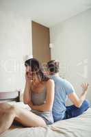 Couple ignoring each other sitting back to back on bed