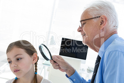 Doctor examining patient ear by using magnifying glass