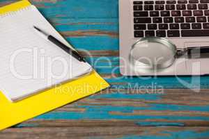 Notepad, pen and magnifying glass with laptop