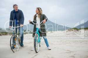 Couple standing on bicycle interacting with each other at beach