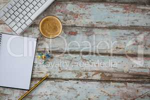 Coffee, pushpin, pencil, computer keyboard and organiser on wooden table