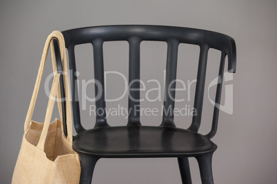 Beige colored shopping bag hanging on black chair