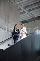Businesswomen discussing over digital tablet while walking on staircase