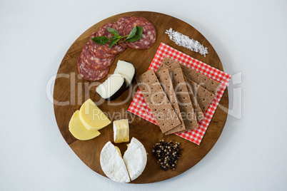 Variety of cheese with salami, crackers, spices and sea salt on wooden board
