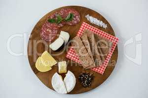 Variety of cheese with salami, crackers, spices and sea salt on wooden board