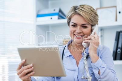 Doctor talking on telephone while using digital tablet