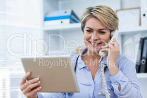 Doctor talking on telephone while using digital tablet