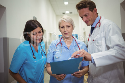 Team of doctors having discussion over file in corridor