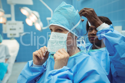 Female surgeon helping her co-worker in wearing surgical mask