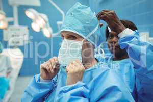 Female surgeon helping her co-worker in wearing surgical mask