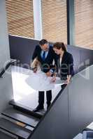 Business colleagues discussing on blueprint while standing on staircase