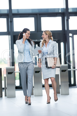 Businesswoman walking with colleague while talking on mobile phone