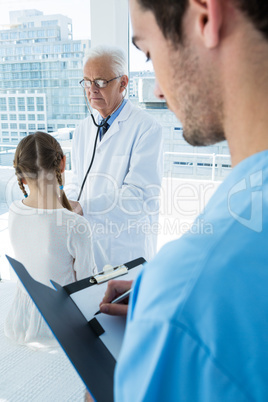 Surgeon writing on clipboard while doctor examines the patient