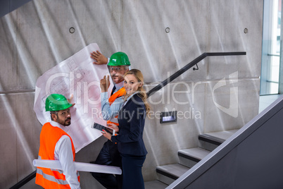 Businesswoman and architects standing on a staircase discussing with blueprint