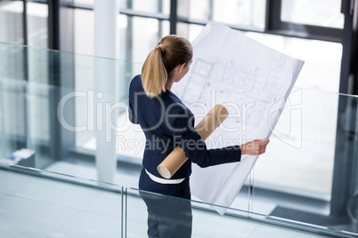 Businesswoman standing at office corridor with blueprint