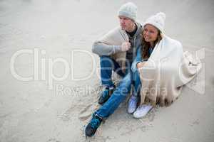 Couple wrapped in shawl sitting on sand
