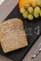 Slices of brown bread, grapes and gouda cheese on slate board