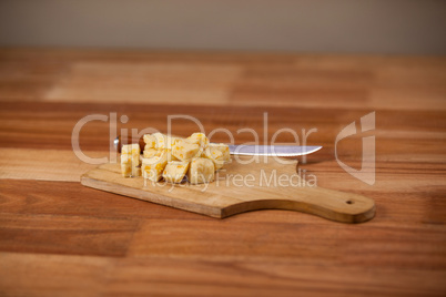 Cheese cubes and knife on wooden chopping board