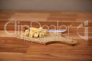 Cheese cubes and knife on wooden chopping board
