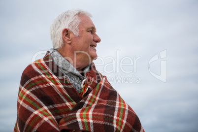 Thoughtful senior man wrapped in shawl at the beach