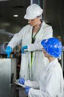 Female technician writing on notepad while examining meat processing machine