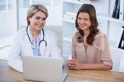 Portrait of smiling female doctor and patient sitting at desk