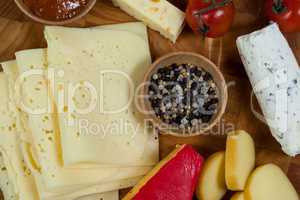 Different types of cheese, cherry tomato, spice and jam on wooden board