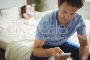 Man using mobile phone while woman sleeping on bed