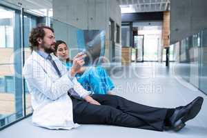 Stressed doctor and nurse sitting on floor examining X-ray report