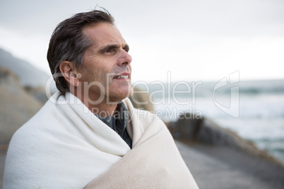 Thoughtful man wrapped in shawl on beach