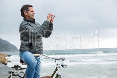 Man on bicycle taking picture on mobile phone