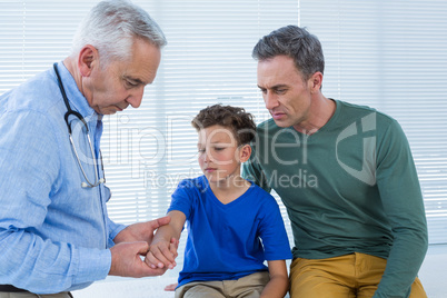 Father looking at sons hand while being examined by doctor