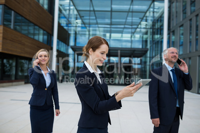 Businesswoman using digital tablet while colleagues talking on mobile phone