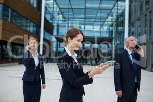 Businesswoman using digital tablet while colleagues talking on mobile phone