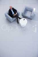 Businessman sitting on sofa with digital tablet and looking up