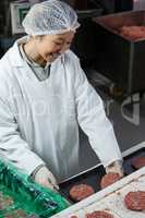 Female butcher arranging hamburger patty on tray