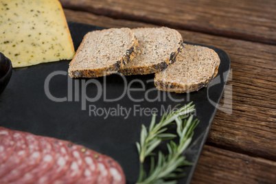 Salami, cheese, rosemary herbs and slices of brown bread on slate plate