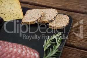 Salami, cheese, rosemary herbs and slices of brown bread on slate plate