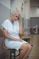 Tensed female nurse sitting on chair in corridor