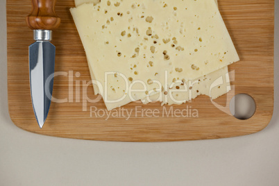 Slices of cheese with knife on chopping board