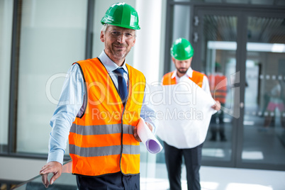 Architect in hard hat standing with blueprint in office corridor