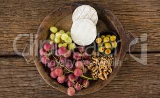 Cheese, grapes, olives and walnut on wooden serving plate