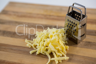 Grated cheese and grater on wooden cutting board